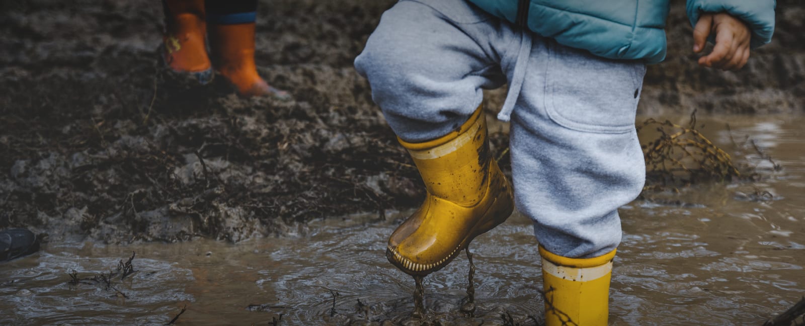 Child wearing yellow wellies jumping in mud